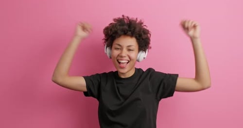 Enthusiastic Woman Dancing with Headphones on Pink Background