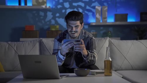 Young Adult Plays Game on Smartphone at Home