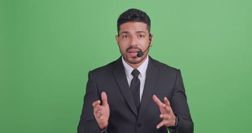 Young male economist wearing a microphone is explaining something. Isolated on green background
