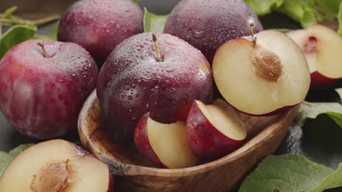 Ripe plums fruits with plum slices slowly move in the wooden bowl.
