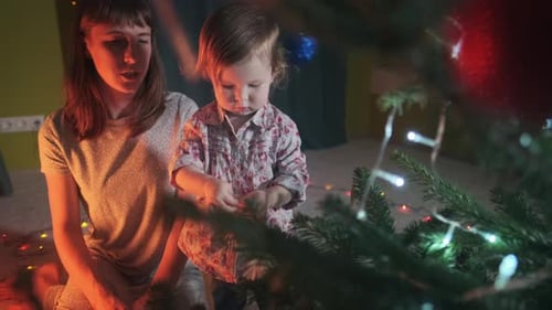 Familie und Weihnachtsbaum. Kleinkind schmückt Weihnachtskiefer mit ihrer Mutter zu Hause