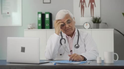 Tired Doctor in Office with Computer and Paperwork