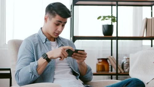 Young Adult Playing Video Games on Phone at Home