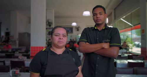 Latin employees stand side by side with arms crossed inside restaurant, showing serious expressions