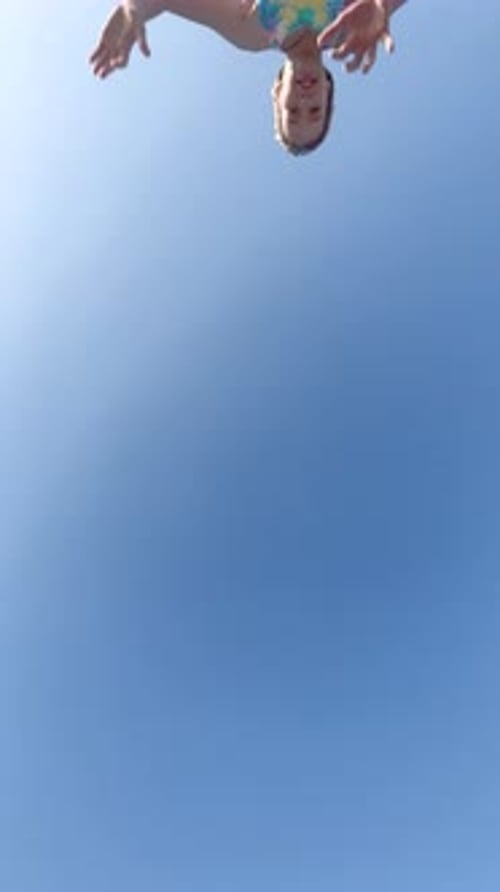 Ein junges Kind am Strand springt mit Salto über die Kameraansicht von unten nach oben