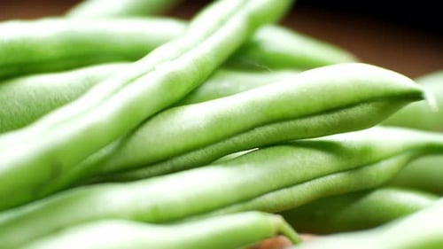 Raw fresh uncooked string beans on wooden kitchen surface close up selective focus dolly left