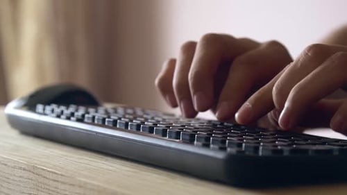 Mãos digitando texto no teclado sem fio na mesa de madeira - de perto