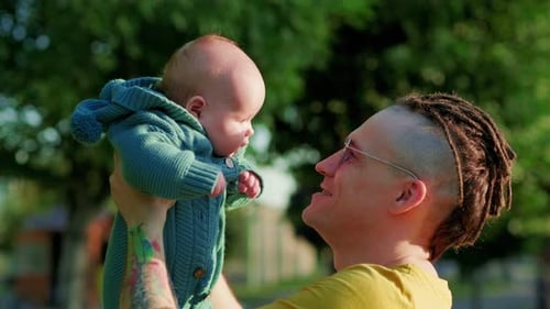 Young Father with His Newborn Baby in the Park on a Sunny Day