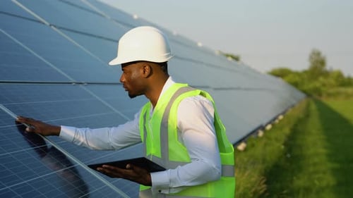 Afroamerikanischer Ingenieur nutzt digitales Tablet, um Solarzellenpaneele zu warten, Techniker bei der Arbeit