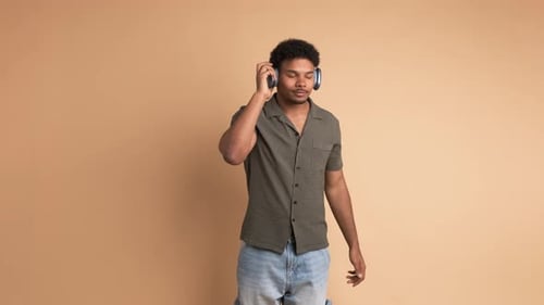 Happy Young Man Enjoying Music with Headphones in Beige Studio
