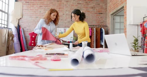 Happy diverse female fashion designers discussing fabrics in studio, slow motion