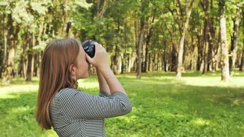 A Young Girl Photographer with a Camera Poses in the Park
