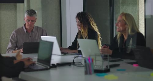 Team working independently on laptops in modern office meeting room with digital display