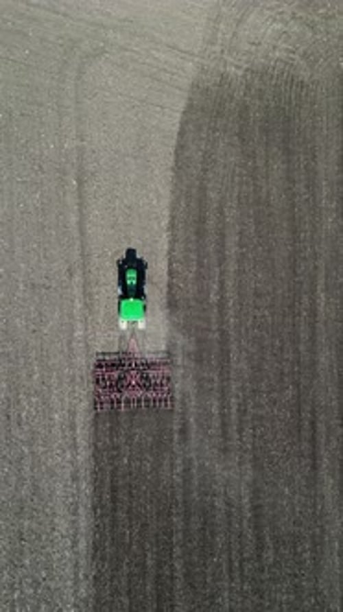 Aerial View of a Tractor Plowing a Large Field Creating Distinct Patterns in the Soil Agricultural