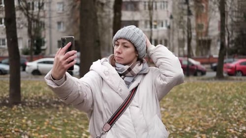 Portrait of Mature Woman in Wool Hat Standing on the Urban Street with Mobile Phone in Hand
