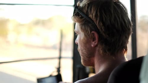 Close up rear shot of red haired man driving the bus during beautiful summer day
