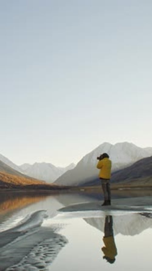 Traveler Taking Photo with Camera By Mountain Lake at Sunrise