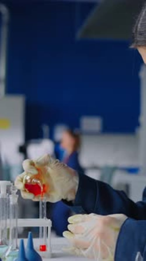 Científico de laboratorio especializado que examina un líquido rojo vivo en un tubo de ensayo de vidrio mientras conduce con cuidado