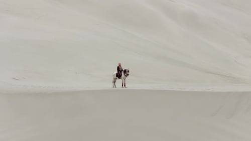 Vue aérienne d'un cavalier seul à cheval dans les dunes de sable du Pakistan avec des montagnes majestueuses