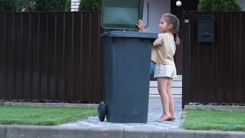 Une petite fille jette un sac poubelle plein dans une poubelle