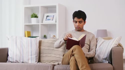 Leisure, Literature and People Concept - Indian Man Sitting on Sofa And