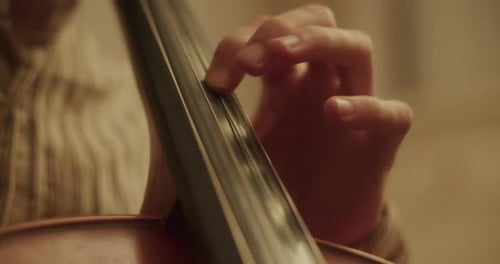 Handheld close up shot of the left hand of a cellist moving over the strings of a cello, doing vibra