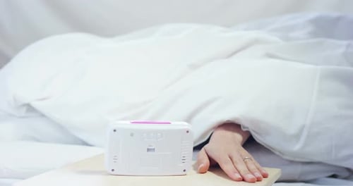 Hand turns off alarm in bed bedroom scene