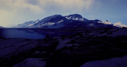 Majestic Mountain Range with Clouds Reflecting on Tranquil Lake at Sunset