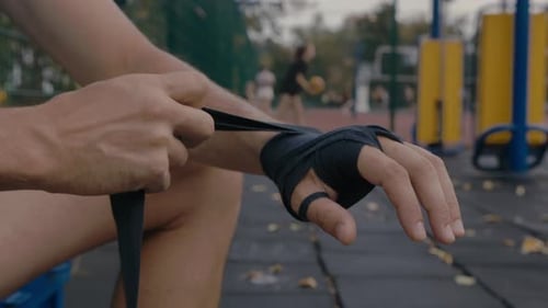Close-up of a man outdoors wrapping his arm in a protective bandage before training before a fight