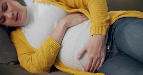 À la maison, enceinte et femme sur le canapé, douleurs et maternité avec maux d'estomac dans le salon