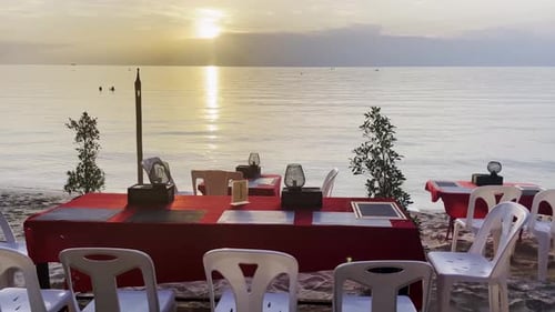 romantic restaurant table set in front of the sea on tropical beach at sunset