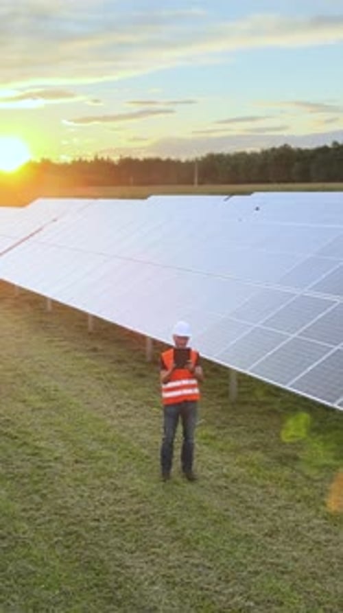 Solar engineer working on a tablet in a photovoltaic solar panel field. Vertical aerial at sunset