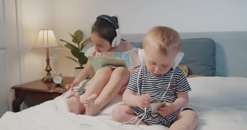 Children Using Mobile Devices and Headphones on Bed