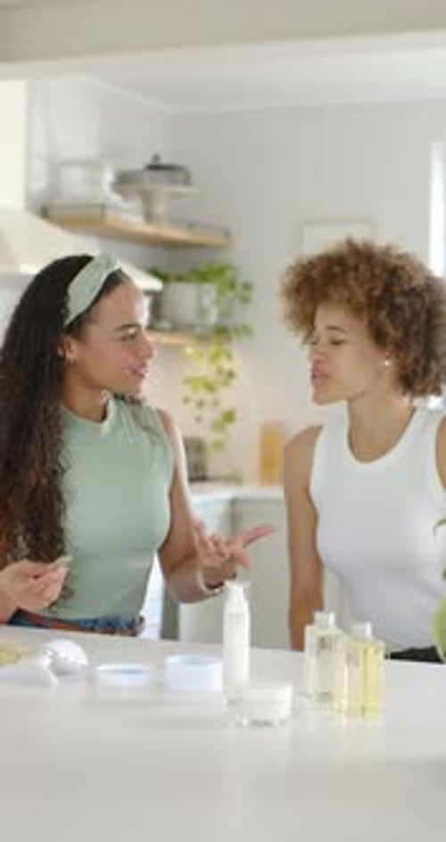 Vídeo vertical: mujeres afroamericanas ven a una amiga izquierda hablando y aplicándose el sérum en el mostrador