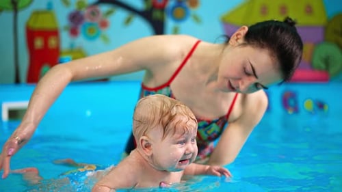 Caucasian woman holding a baby in the pool on her palm. Infant child is taught to swim.