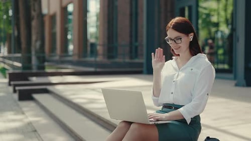 Business Woman Sitting on the Stairs Near the Business Centre and Making Video Call on the Laptop