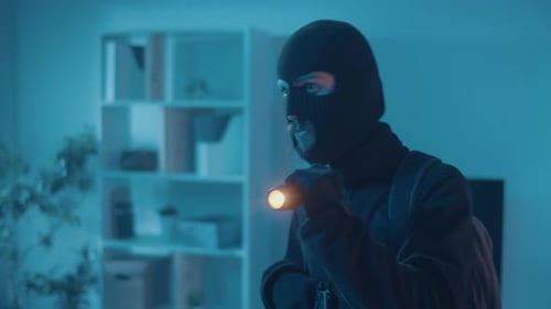 Masked Figure with Flashlight Investigating in Dark Room