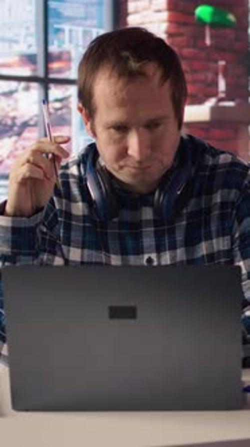 Stressed Man in Home Office Scratching Head with Pen Feeling Overworked