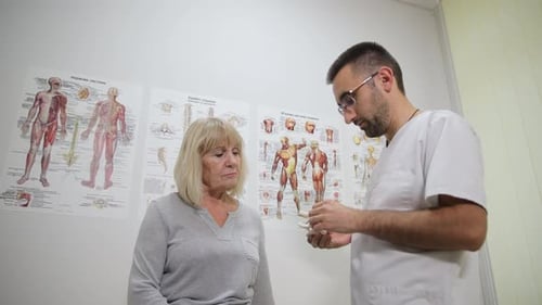 Ein Mann gestikuliert und teilt ein lustiges Ereignis mit einer älteren Frau in einem Krankenzimmer