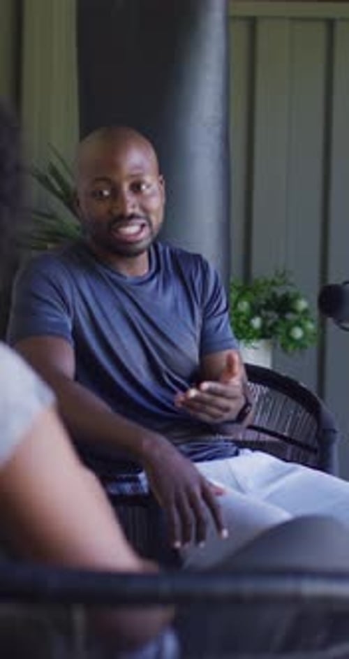 Vidéo verticale : un homme africain en t-shirt bleu marine répond à la question de son partenaire sur le porche, faisant des gestes avec le micro