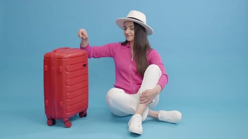 Cheerful caucasian girl in white hat leaving on vacation trip with suitcase, preparing for journey