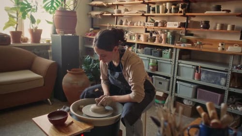 Young Woman Shaping Clay on Pottery Wheel in Cozy Ceramic Workshop