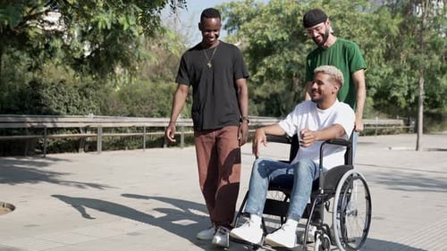 Young Friends Pushing Wheelchair of Disabled Man Having Good Times Together Walking in the City