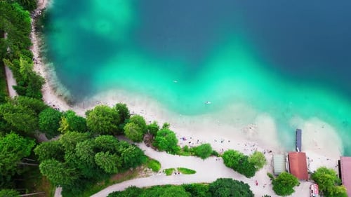 A view from above of a turquoise lake shoreline, lined with trees, with a dock and path leading into