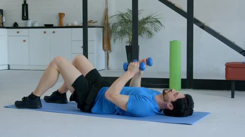 Adult Man Lying on Mat Lifting Dumbbells