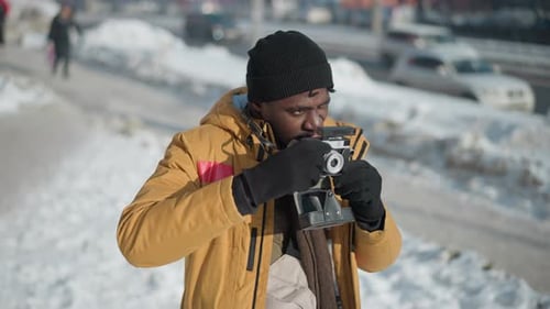 Man Focusing Vintage Camera in Snowy Urban Setting