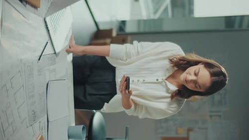 Woman Uses Phone Near Architectural Blueprints in Office