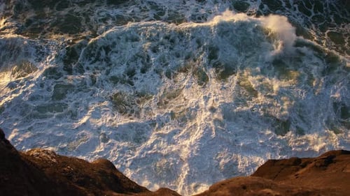 Foaming Sea Waves Crash Against the Rocks in the Golden Hour