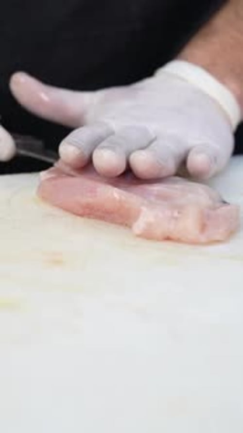 Chef slicing raw chicken fillet with knife