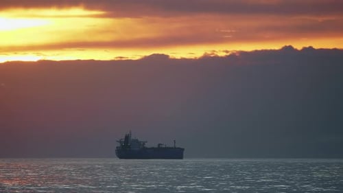 Steady shot of a cargo ships sailing in a calm ocean near port in Portugal. Sunset and dark clouds.
